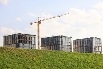 Defocused view to unfinished residential buildings and construction crane from hill with green...