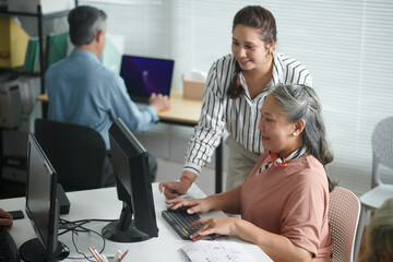 Smiling teacher helping elderly woman to send e-mail and install application on computer