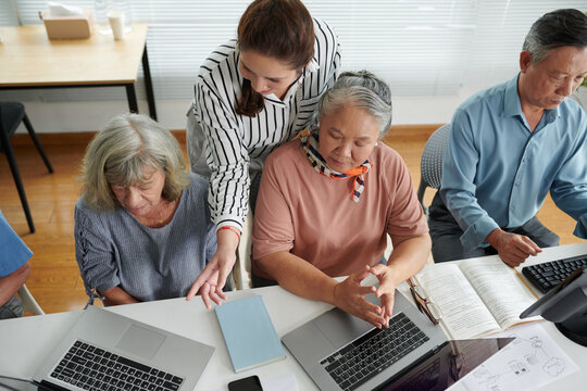 Young Woman Helping Confused Elderly Women To Launch Program On Laptops