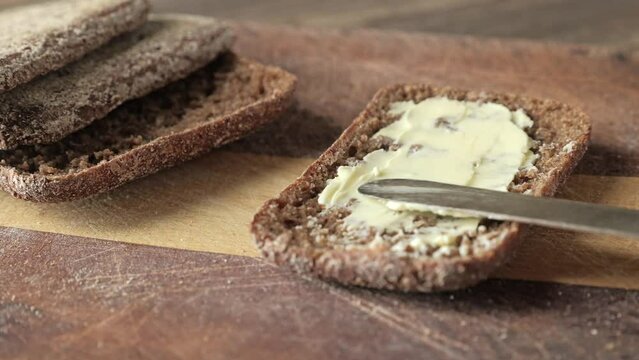 Close-up of spreading butter on a slice of rye bread with a vintage knife.