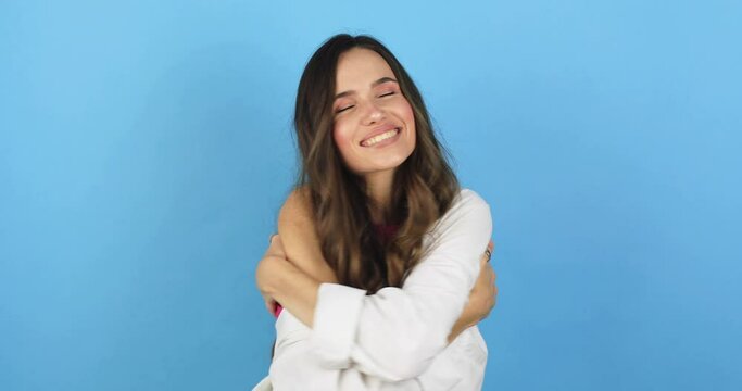 Come into my arms. Adorable happy girl with brown hair in pink top gesturing come here for free hugs and smiling sincerely with welcoming expression isolated on blue background. Come to me, hug self.
