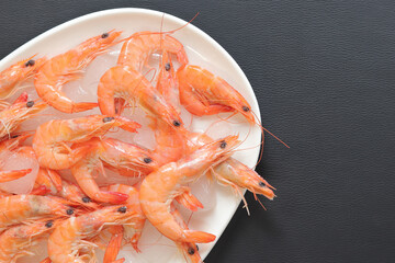 Fresh chilled shrimp in a white plate with ice on a gray background. Boiled shrimp in a plate with ice, top view. Seafood on crushed ice. Healthy eating concept