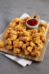 Homemade Crunchy Popcorn Chicken with Ketchup on a Board, side view.