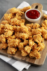Homemade Crunchy Popcorn Chicken with Ketchup on a Board, side view.
