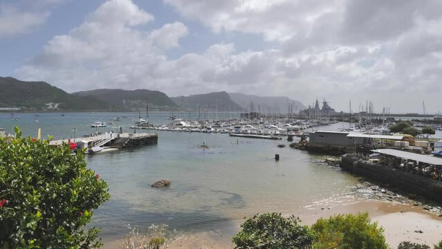 Simon's Town harbour, pier and yacht club viewed from shore. Fish Hoek mountains and naval ship in background
