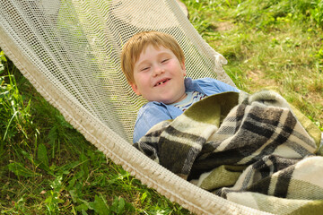 Boy's joyful escape in a garden hammock, wrapped in comfort, smile radiating peace. A tranquil...