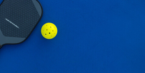 Pickleball tennis racket on the court. Blue background with copy space. Sport court and ball.