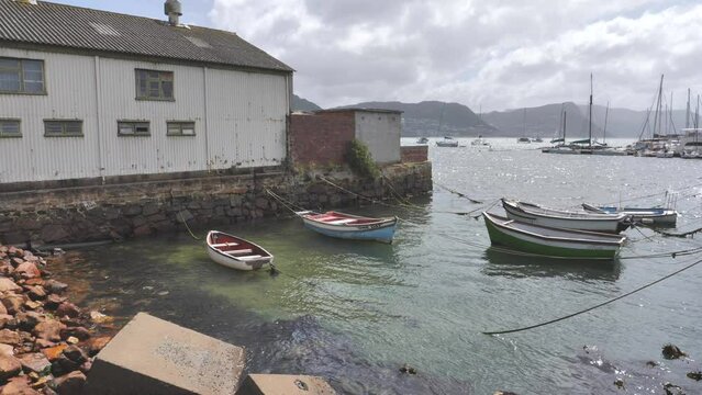 Small fishing boats moored to stone wall below old corrugated iron building near Simon's Town yacht club