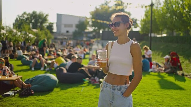 Portrait of beautiful young woman drinking beer and enjoying summer day. woman holding plastic glass with beer. party time outdoors. Happy hour, lunch break and youth concept