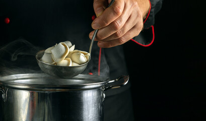 Professional chef preparing dumplings in a saucepan in the restaurant kitchen. Close-up a ladle...