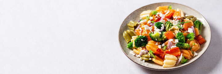 Autumn pasta salad with roasted pumpkin, broccoli, feta cheese on bright light background, fall season salad