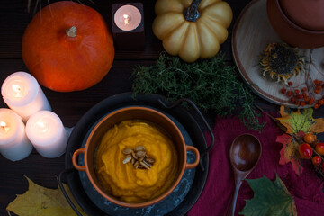 Obraz premium Autumn pumpkin soup-puree on a wooden table with a whole pumpkin. Romantic candlelit dinner, dry spikelets Village Concept