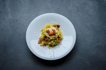 typical italian pasta carbonara recipe, with bacon, eggs, and fresh gomemade pasta in white plate on grey wallpaper, vertical view, closeup