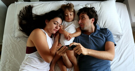 Millennial couple in bed with baby toddler infant boy watching content on cellphone device