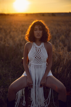 fashion portrait of a curly-haired woman in white clothes dress sit on a field with dry grass in autumn.