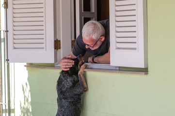 elderly man petting a dog at home window