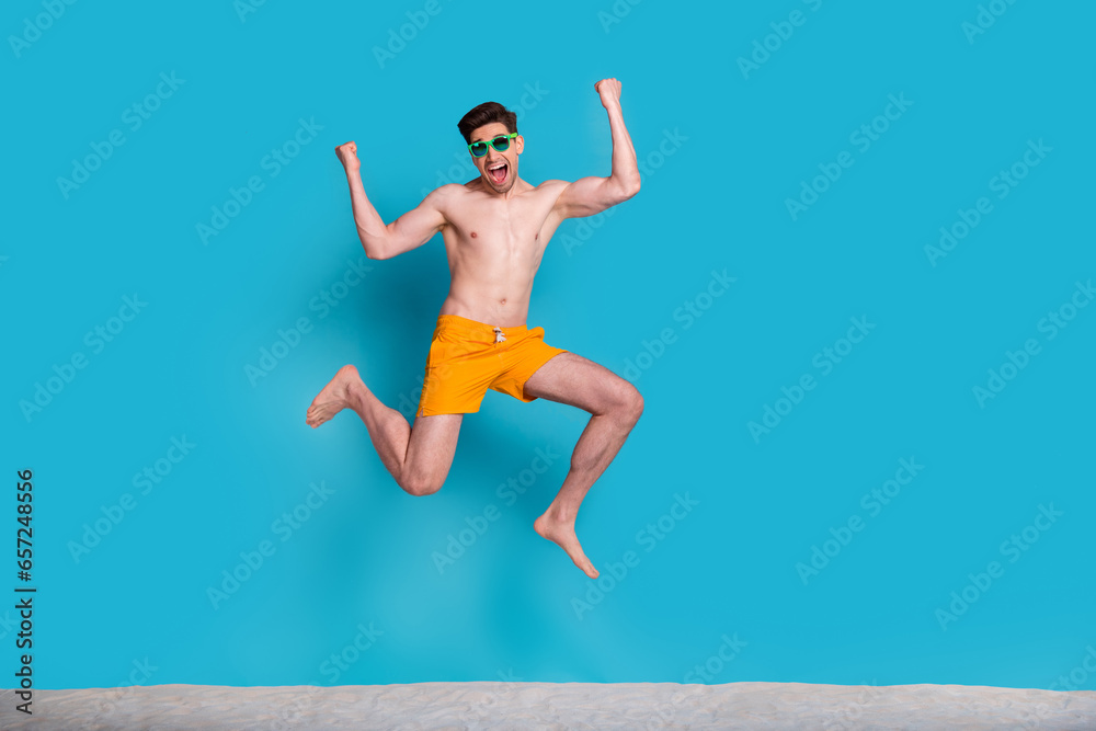 Poster Full body photo of handsome young guy excited jump raise hands wear trendy yellow shorts isolated on blue color background summer vacation