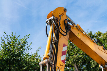 Part of the boom of an orange excavator with a hydraulic drive against a background of blue sky and...