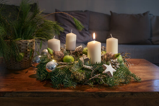 First Advent, wreath with one burning white candle and Christmas decoration on a wooden table in front of the couch, festive home decor, copy space, selected focus