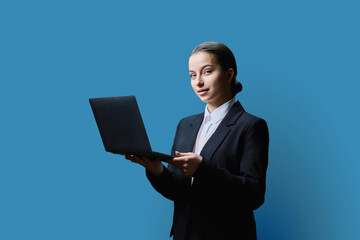 Teenage female student in formal style using computer laptop, on blue background