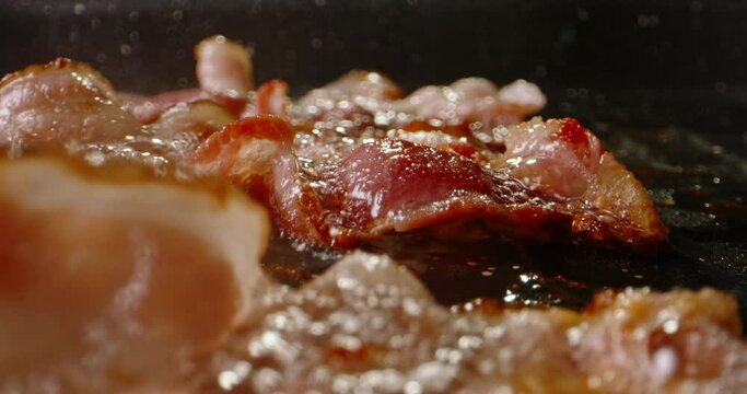 Frying halal beef bacon in pan side view macro shot slow motion. Classic breakfast spread, complete with bacon's irresistibly smoky and crispy goodness. Start the day with traditional breakfast. Fat