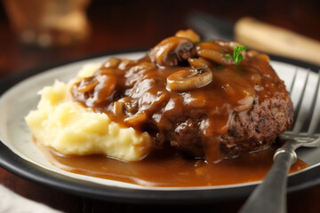 Delicious home cooked Salisbury steak with thick luscious brown mushroom gravy served with mashed potatoes on a plate. Traditional American cuisine dish specialty for family dinner holiday celebration - obrazy, fototapety, plakaty