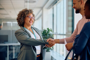 Happy insurance agent shaking hands with young couple as they meet in office.