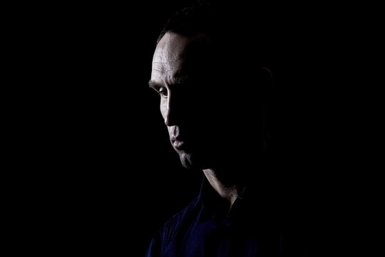 Portrait of a thoughtful man with chiaroscuro, a rocky and convex face, alone in the dark, with high contrast