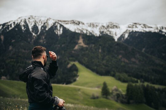 Chico con c&aacute;mara en la mano observando paisaje de monta&ntilde;as nevadas y prado verde .