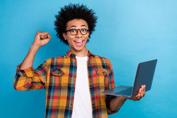 Photo of mixed race guy with perming coiffure wear checkered jacket holding laptop win bet scream yeah isolated on blue color background