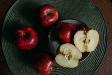 Red, ripe, fresh, juicy apples. Five apples on the table, one apple cut into two halves. Three apples on the table, two apples in a grey plate. There's a green napkin under the plate