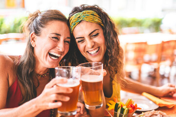 Happy women having fun drinking beer outdoors at pub terrace, Two girls friends toasting glass of pint at brewery pub enjoying food, Social Lifestyle concept with happy young people