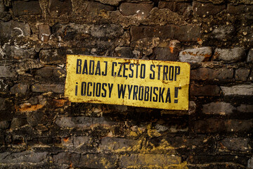 A warning sign in Polish in an underground corridor: examine the ceiling and sides of the excavation frequently!