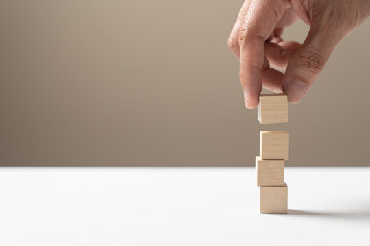 Hand arrange four empty wooden cube blocks stack on white table.