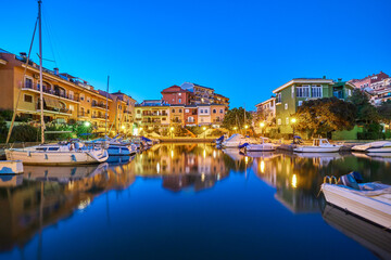 Fototapeta na wymiar Panoramic view of colorful houses and moored yachts in the evening in Port Saplaya. Light from street lamps, buildings and boats reflects on the smooth surface of the water. Valencia's Little Venice.