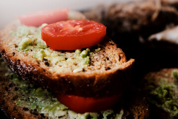 Avocado sandwich and tomato. Black bread with avocado and a close -up tomato. Healthy diet