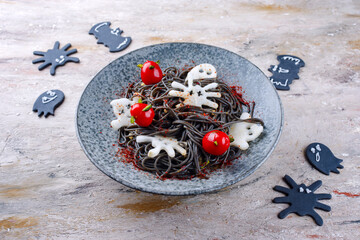 Traditioneller Halloween Tintenfisch Spaghetti mit Dracula Spinnen, Fledermäuse und Bluttropfen Tomaten serviert als close-up in einem Nordic Design Teller
