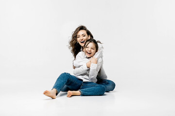 Fototapeta na wymiar Young mother and little girl playing on a white background. The concept of advertising positive, happy sincere emotions, clothes and a happy carefree life.