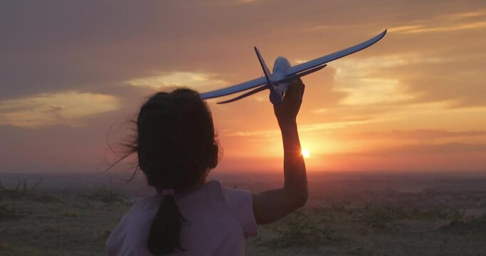 Silhouette of happy kid girl running with a toy airplane at sunset. Happy kid in nature. Children dream. Silhouette shot