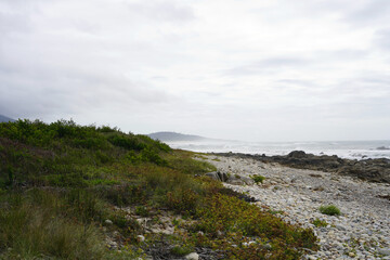 Landscape by the sea. We see a rocky beach and a distant view through the fog.