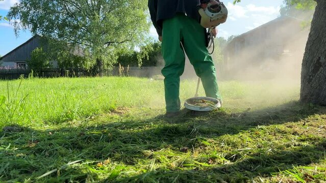Grass Trimmer and Grass Cutter. lawn maintenance service. Gardener mows weeds grass. Man cutting grass in yard by using string trimmer. Worker lawn mower cutting garden. Lawn mowing machine. 