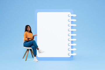 Positive young black woman in casual sit on chair point hands on big plan list with free space - obrazy, fototapety, plakaty