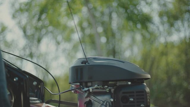 Close-up view of a gardener wearing gloves manually starting a lawn mower in garden on the grass. Shot in slow-motion