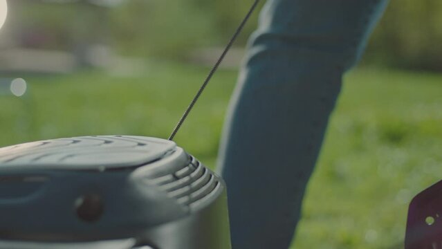 A close-up shot of a man starting a lawnmower in his garden. Shot in slow-motion