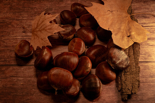 Chestnuts on a wooden table with dry leaves and a piece of bark