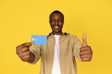 Happy young african american guy in casual show credit card and thumb up gesture with hand
