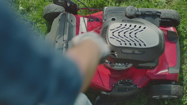 Man gardener starting motor, engine of a lawnmower at the backyard garden, summer work in garden, cutting green grass