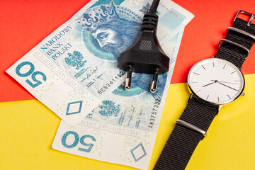 cable with plug, Polish zloty banknotes and watch lying on yellow-red background (selective focus)