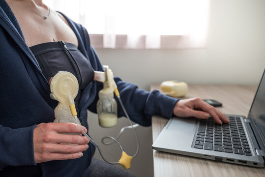 Mother or mom worker pumping breastmilk using an Automatic breast pump device with nursing bra while typing on laptop pc computer on table. Motherhood in corporate office. Mother working from home