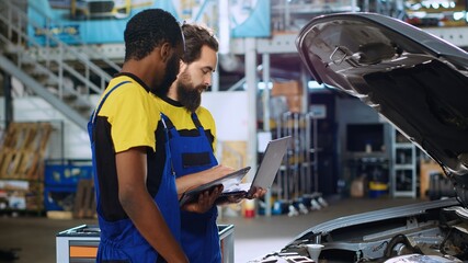 Qualified repairmen in car service ordering new parts for damaged vehicle using laptop and tablet....